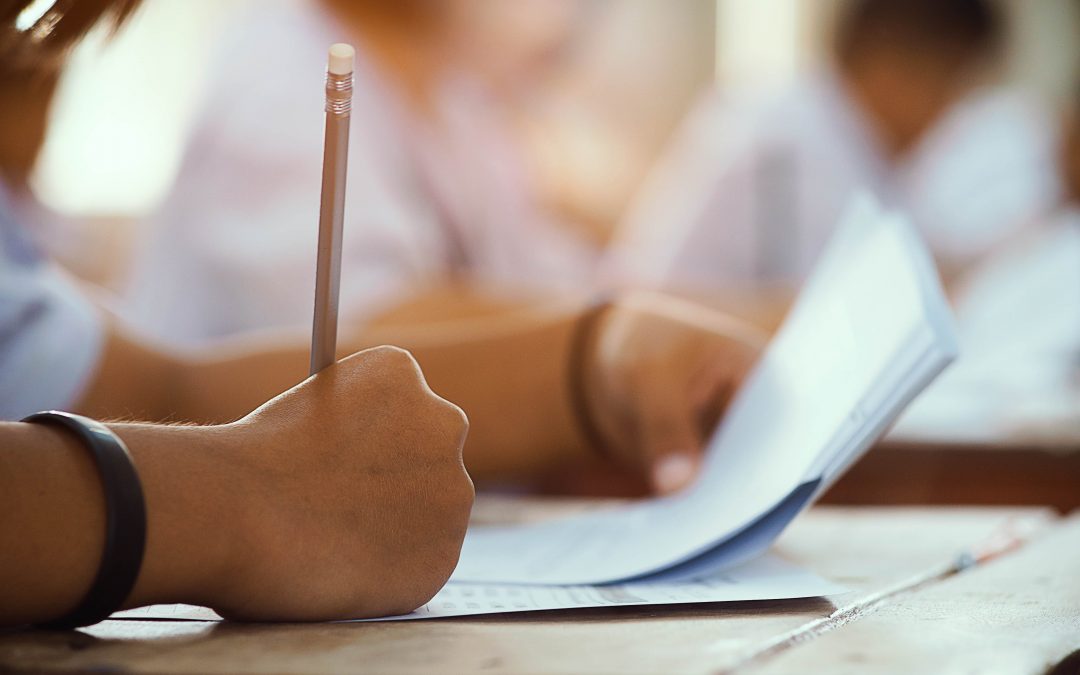 closeup to hand of student holding pencil and taking exam in classroom with stress for education test